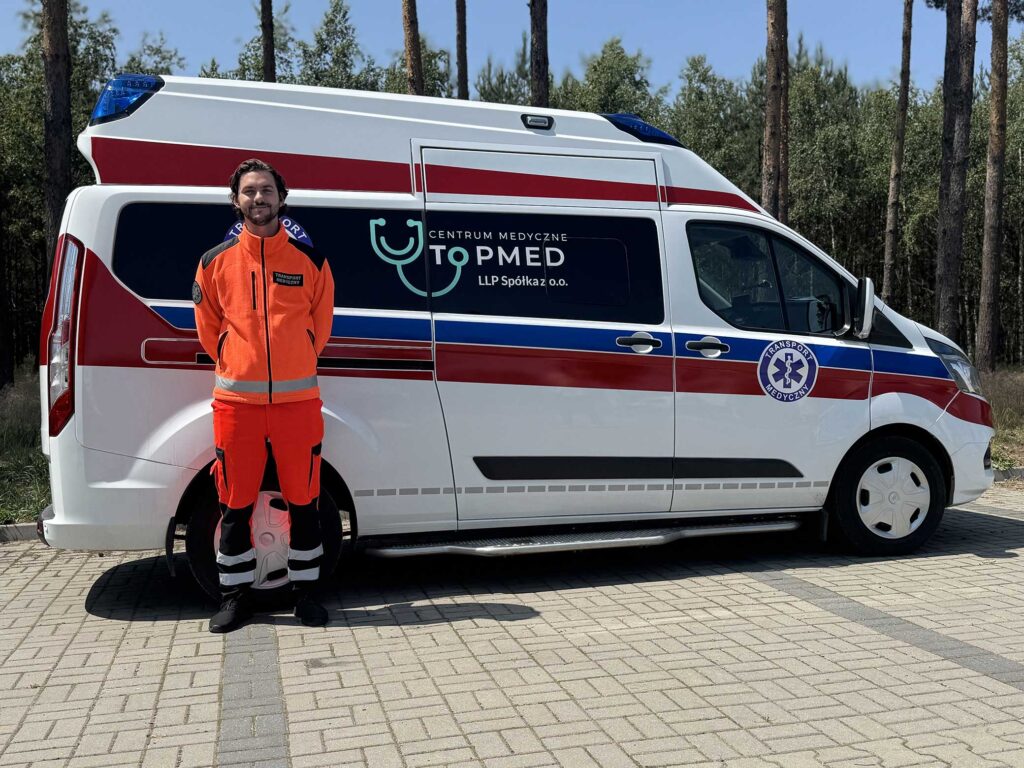 ratownik medyczny w pomarańczowym stroju stoi przed bokiem karetki